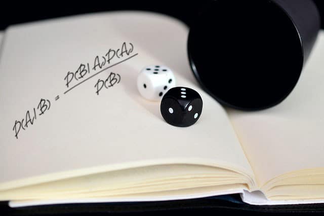 Bayes' theorem hand-written on a notebook. Additionally, two dice are rolled on top of the notebook from a black plastic cup.