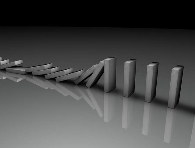 The domino effect illustrated with gray domino tiles in the process of falling one by one.