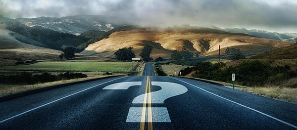 A curvy road with a question mark leading to a cloudy mountain